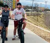 Three individuals are cycling along a path with a cityscape in the background