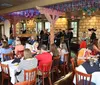 This vibrant image depicts people enjoying outdoor dining by a canal with colorful umbrellas and a bridge in the background beneath a large abstract sculpture