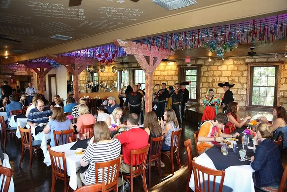 Guests are dining in a festively decorated room while being entertained by a group of mariachi musicians