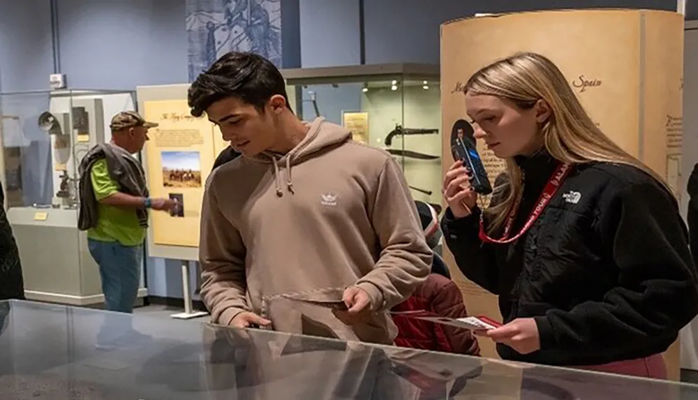 Two young people are engaged in an educational activity at a museum exhibit while a person in the background views another display