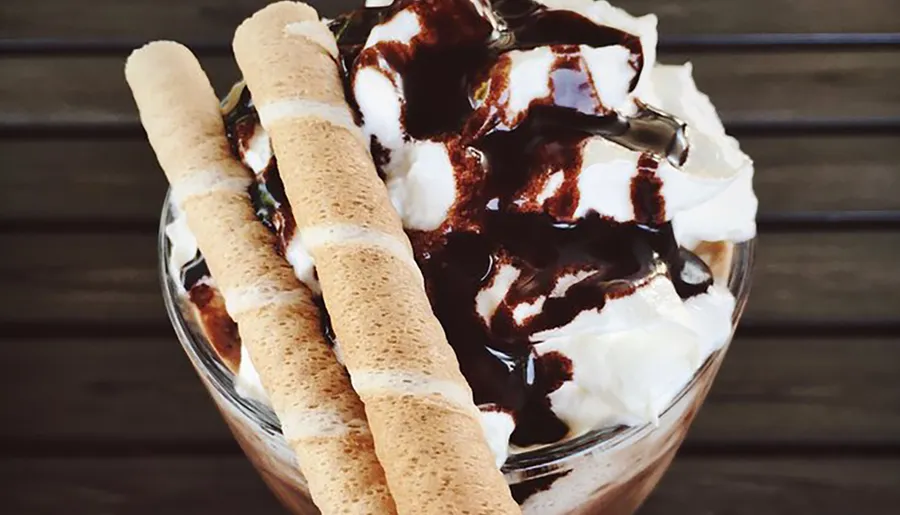 The image shows a delicious-looking dessert with whipped cream, chocolate syrup, and wafer sticks.