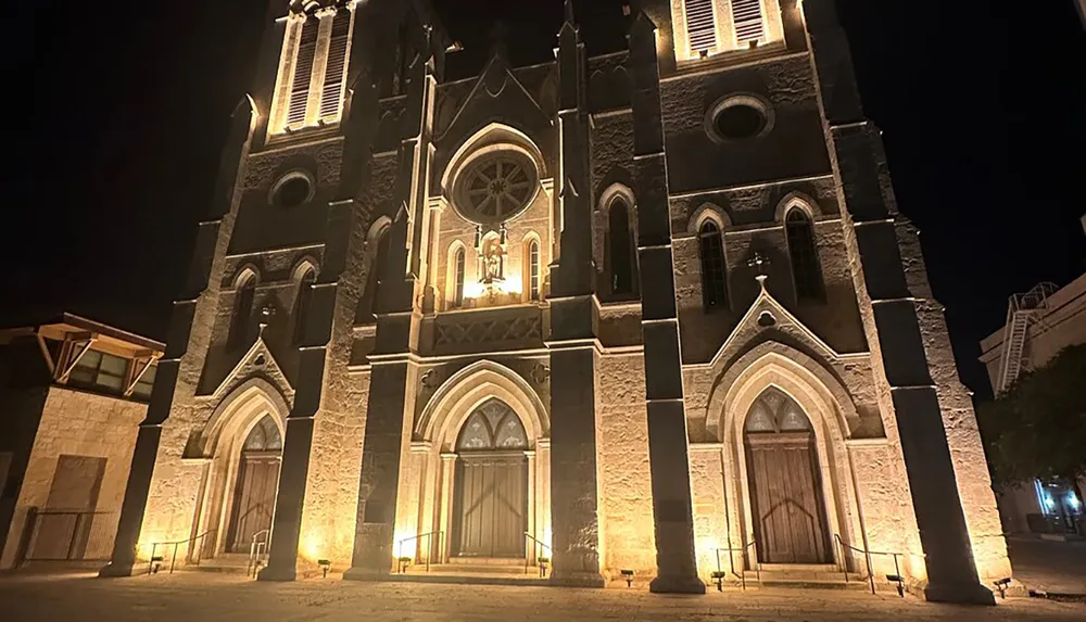 The image shows the illuminated facade of a Gothic-style church at night creating a dramatic and historic architectural scene