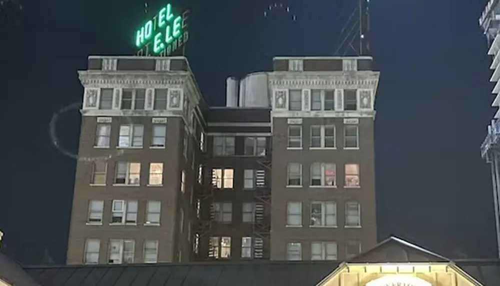A nighttime image of a multi-story building with the neon sign HOTEL lit at the top and windows illuminated in various rooms