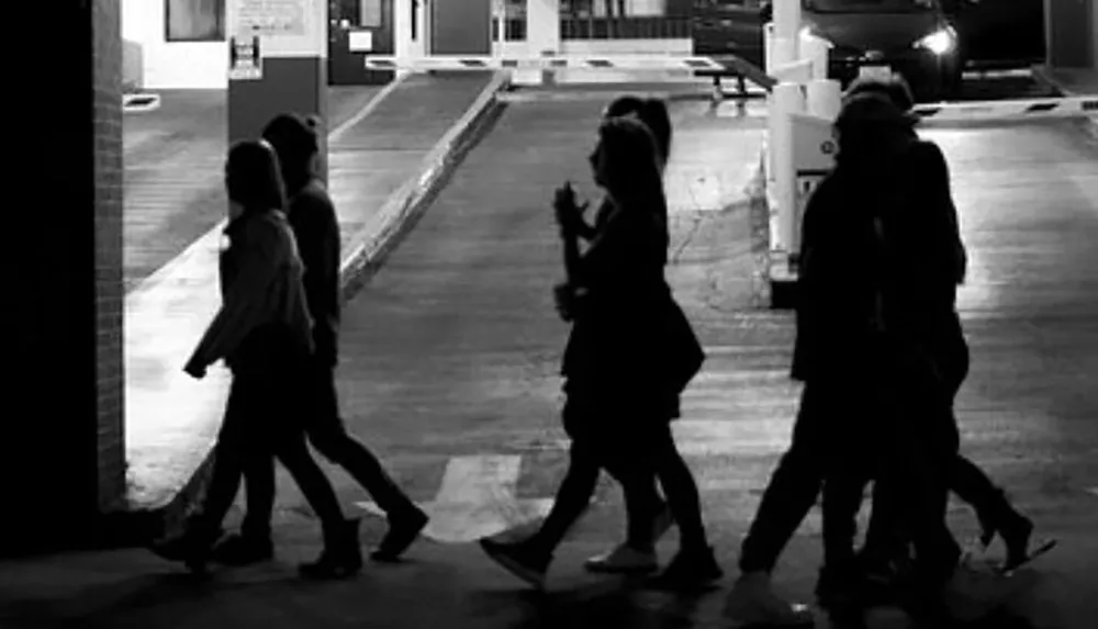 A group of people is captured in silhouette as they walk across a parking lot at night