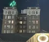 The image appears to be a nighttime view of a cityscape featuring the upper floors of a traditional building with a glowing Hotel neon sign on its rooftop and the partial faade of a foreground building with a sign that reads Franklins