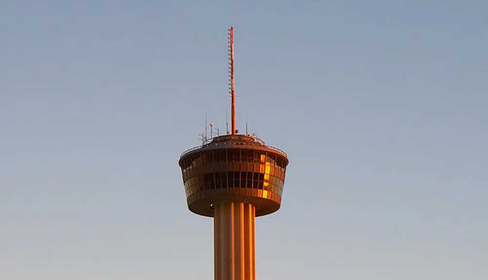 The image captures the upper section of a tall observation tower bathed in warm sunlight against a clear sky