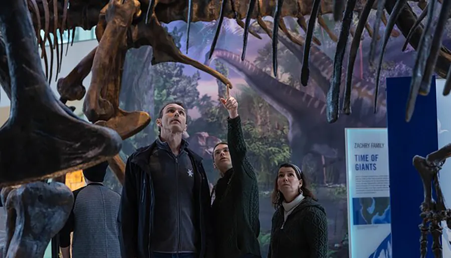 Visitors are examining a dinosaur skeleton on display in a museum exhibit entitled Time of Giants.