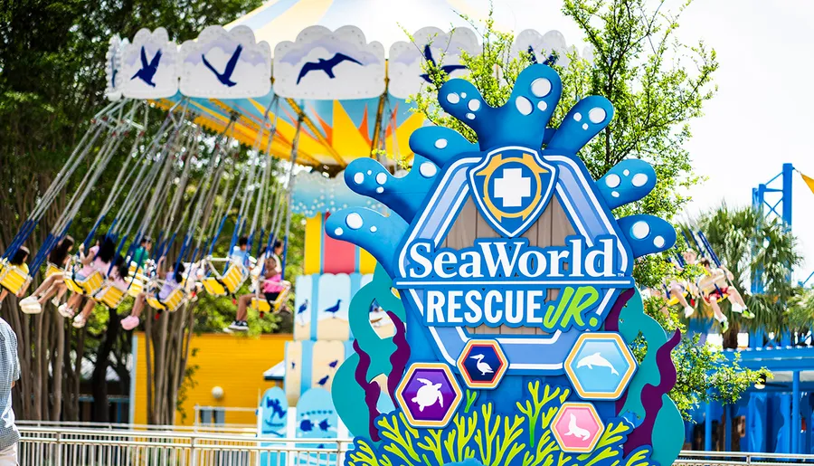The image shows a colorful ride at SeaWorld with a sign for SeaWorld Rescue Jr. in the foreground.