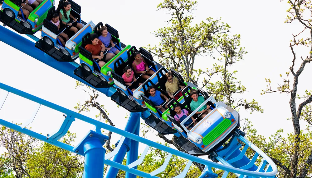 A group of people are enjoying a thrilling ride on a colorful roller coaster against a backdrop of trees