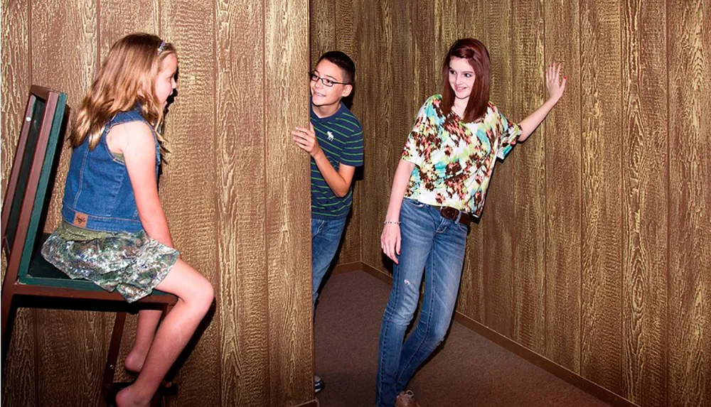 Three individuals appear to interact with an Ames Room illusion creating a distorted perception of their relative sizes