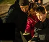 A group of people is gathered around a lantern listening intently to a person where the hoodie indicates they are probably on a ghost tour