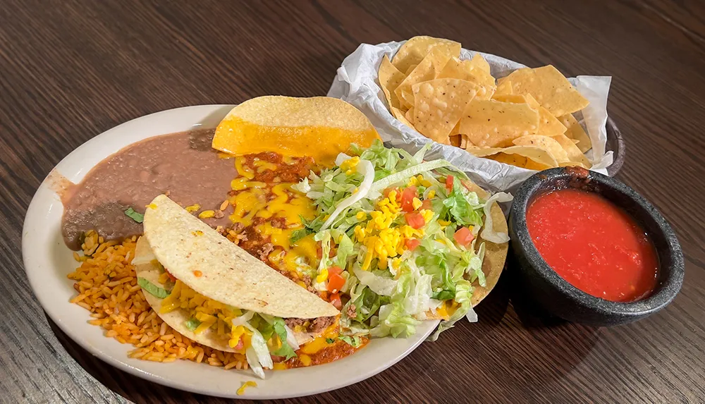 This image features a plate of Mexican food including tacos with side servings of rice beans tortilla chips and salsa