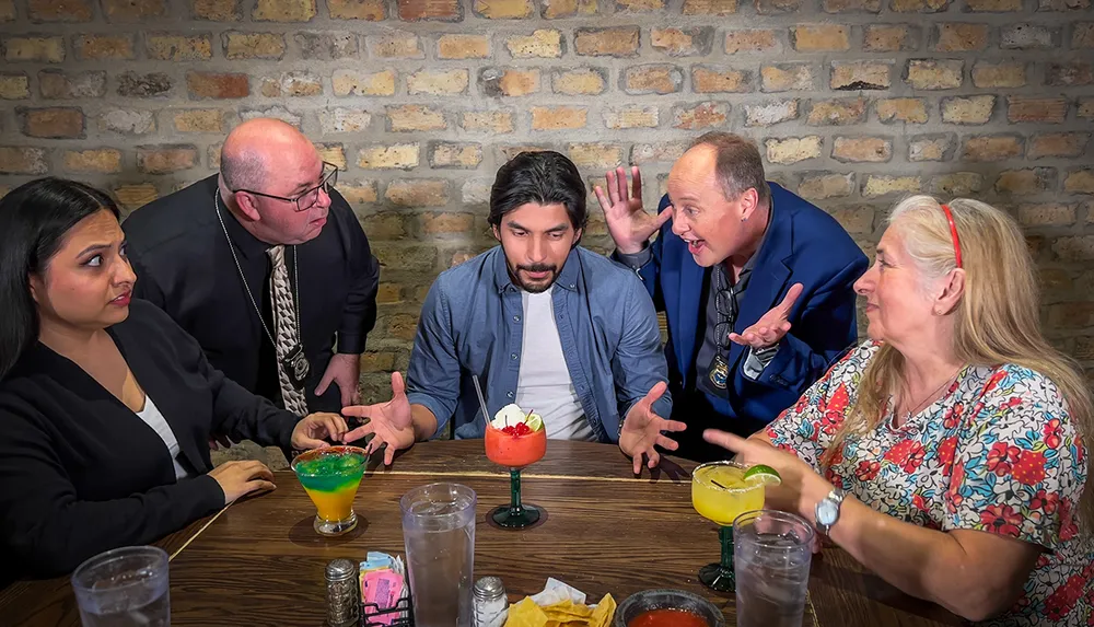 A group of people is engaged in an animated conversation at a dining table with drinks and chips showing a variety of emotions and gestures