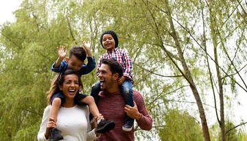 A happy family with two adults and two children are enjoying their time outdoors, with the children sitting on the adults' shoulders.
