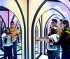 Several people navigate a colorful and reflective mirror maze with vibrant lights creating a kaleidoscopic effect
