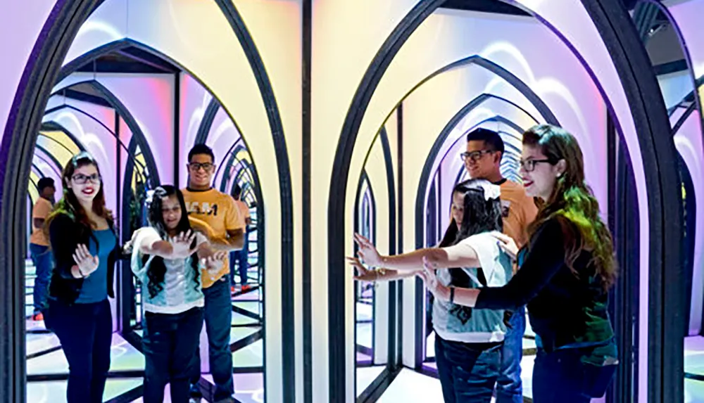 A group of people are exploring a colorful mirror maze creating reflections that give the illusion of endless arches and pathways