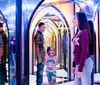 Several people navigate a colorful and reflective mirror maze with vibrant lights creating a kaleidoscopic effect