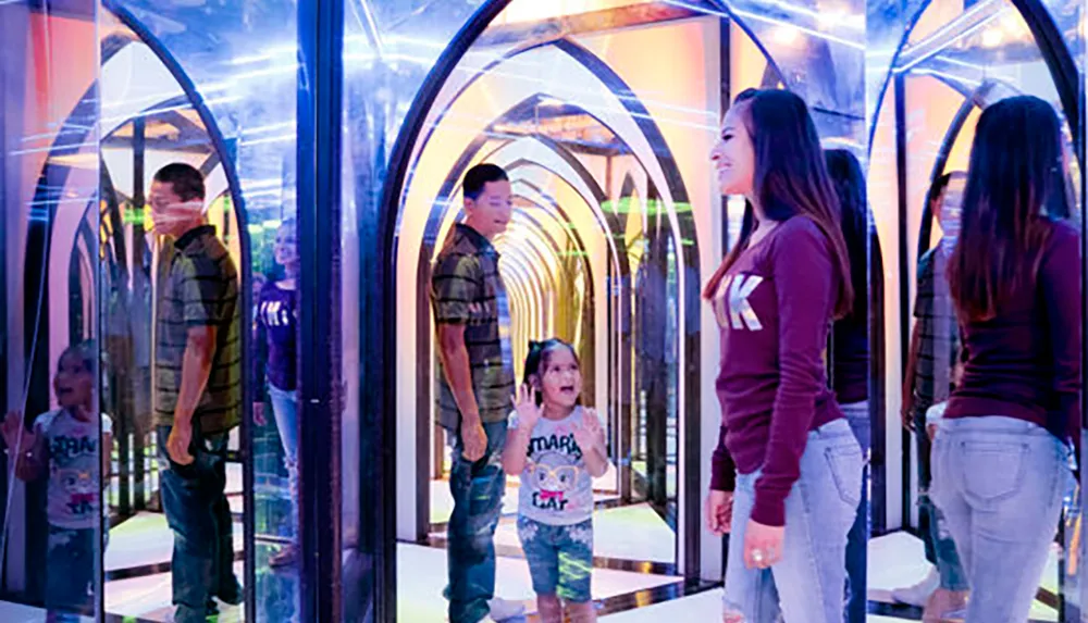 A family is having fun navigating a colorful mirror maze with reflections all around them