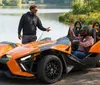 The image shows two Polaris Slingshot three-wheeled vehicles driving down a scenic road with passengers wearing helmets