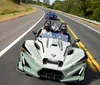 The image shows two Polaris Slingshot three-wheeled vehicles driving down a scenic road with passengers wearing helmets