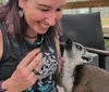 A woman with tattoos and jewelry is smiling at a lemur looking up at her