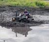 A person in full protective gear is riding a red ATV on a dirt trail kicking up dust and mud