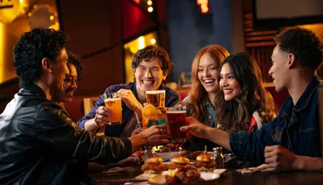 A group of joyful friends is toasting with drinks at a restaurant table filled with food.