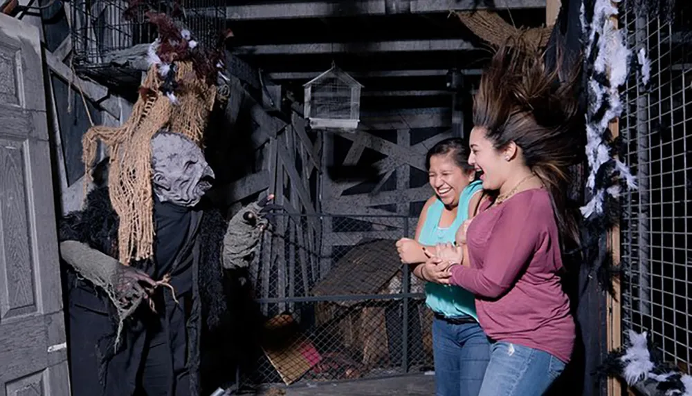 Two people are laughing and seemingly startled by a disguised figure at what appears to be a haunted attraction