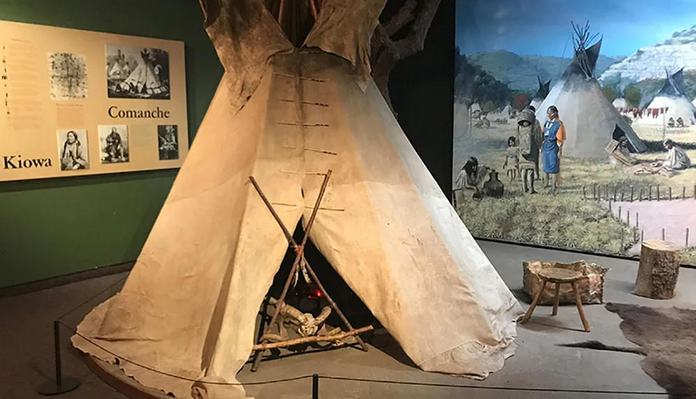The image shows a museum exhibit featuring a tipi artifacts and informative displays about the Comanche and Kiowa peoples