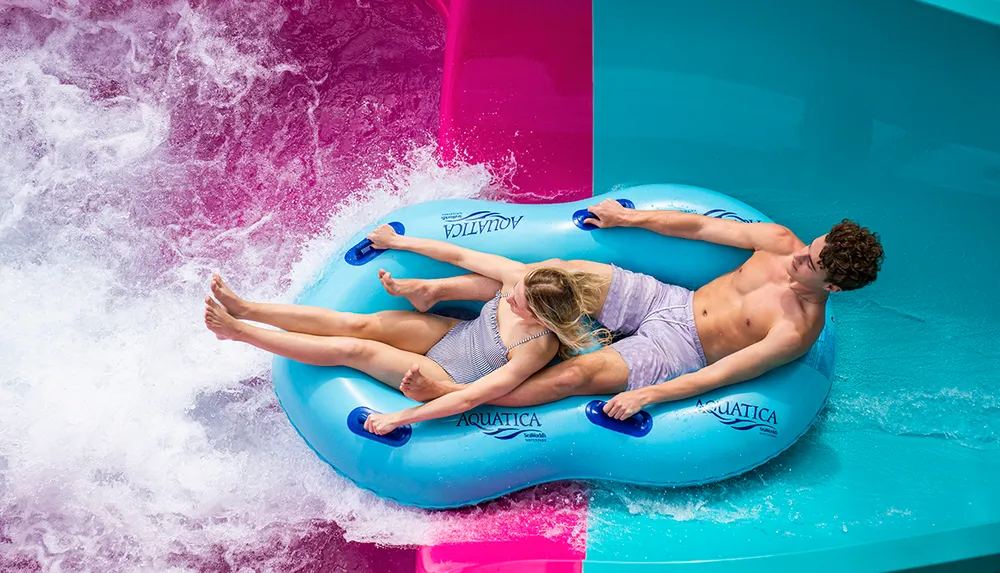 Two people are enjoying a water ride on a blue inflatable raft at a water park