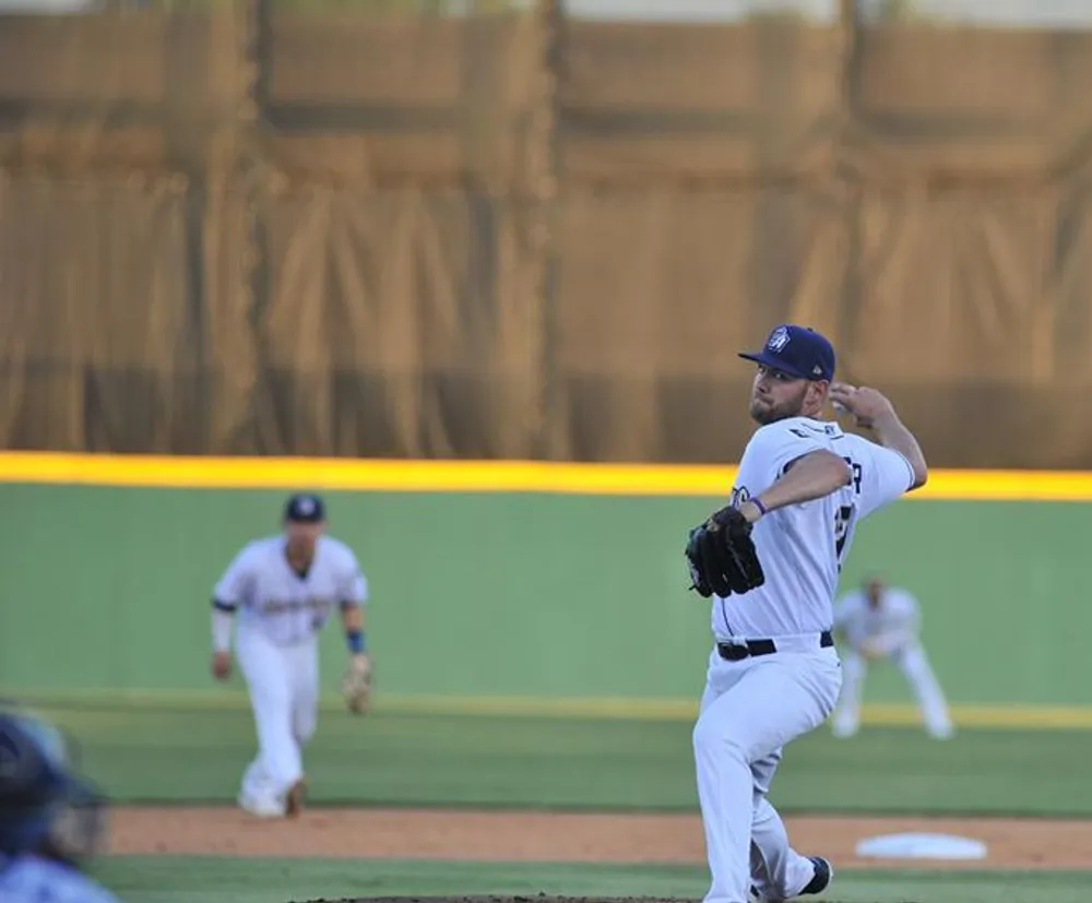 A baseball pitcher is in the middle of a throwing motion on the field while teammates are positioned in the background