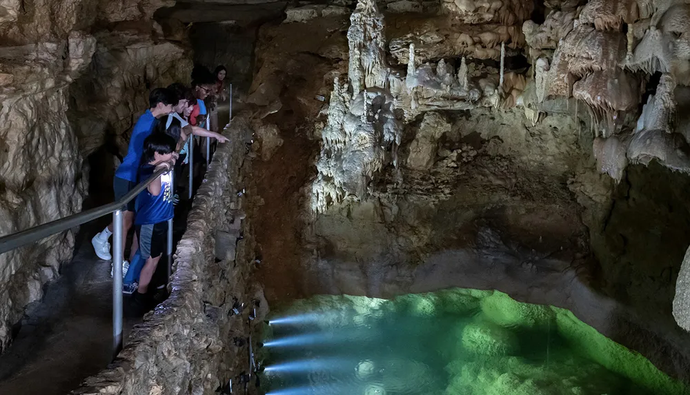 Visitors are exploring a naturally illuminated cave with a clear pool of water and intriguing rock formations