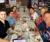 A group of smiling people is gathered around a dining table in what looks to be a casual restaurant setting suggesting a social or familial gathering