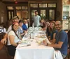 A group of smiling people is gathered around a dining table in what looks to be a casual restaurant setting suggesting a social or familial gathering