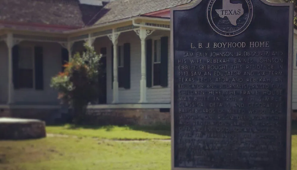The image features a historical marker in front of a traditional American house commemorating it as the boyhood home of President Lyndon B Johnson