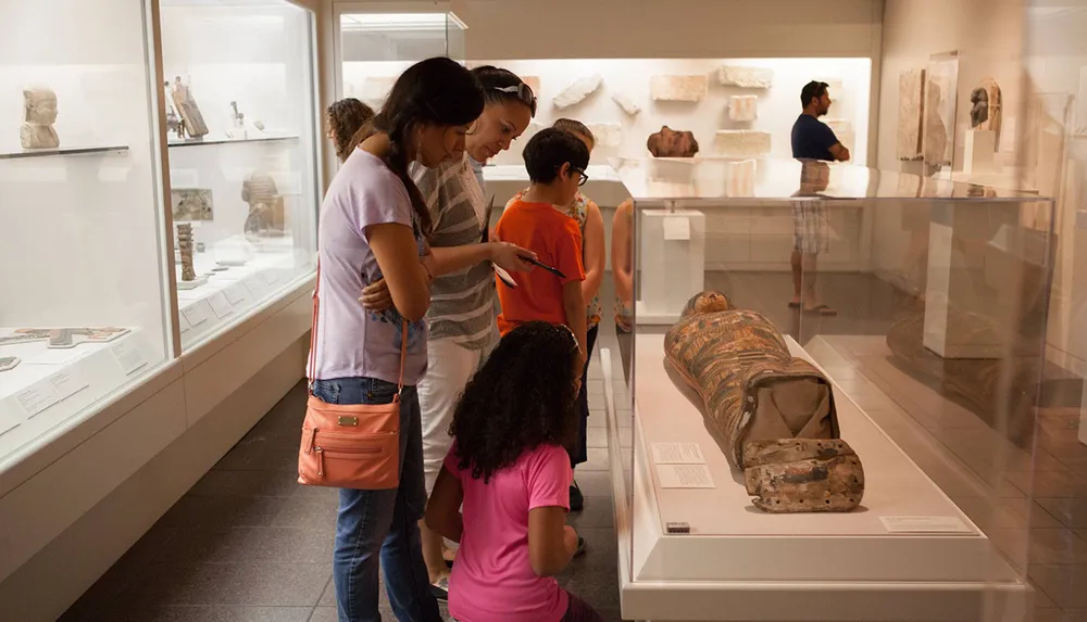 Visitors are closely examining ancient artifacts at a museum exhibit with a focus on a sarcophagus