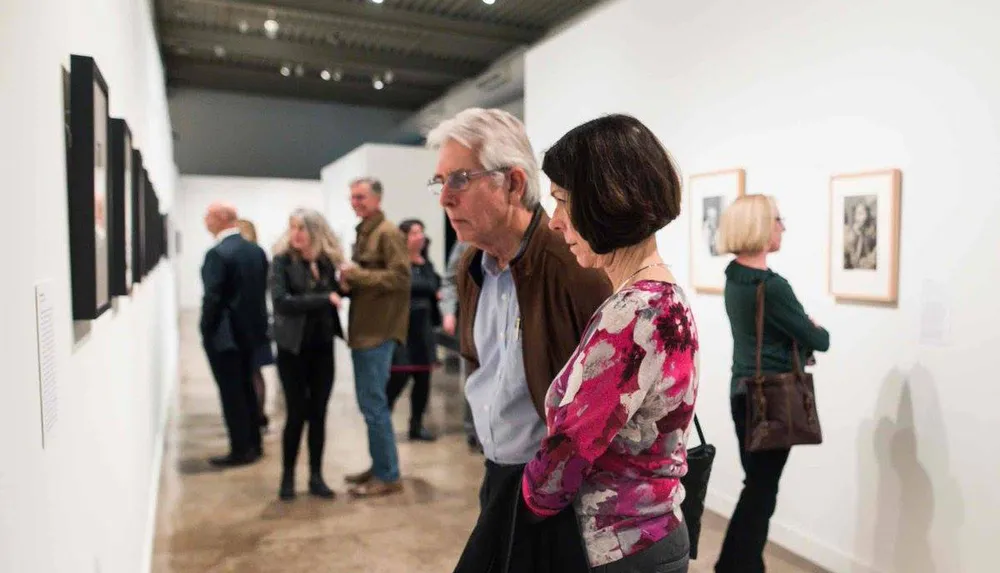 A group of people are attentively viewing and discussing various artworks displayed on the walls of an art gallery