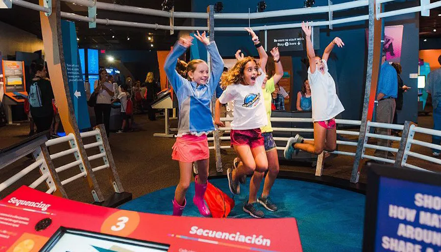 Three children are joyfully jumping and celebrating inside a vibrant science museum or interactive learning space.