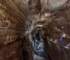 Three joyful individuals are posing with arms raised in a cave-like setting expressing happiness or excitement