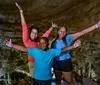 Three joyful individuals are posing with arms raised in a cave-like setting expressing happiness or excitement