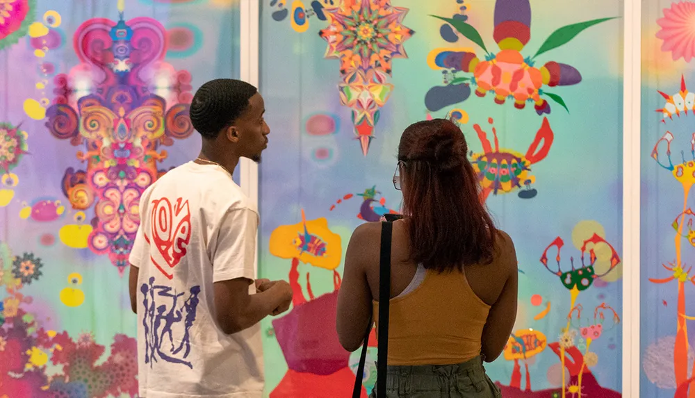 Two people are viewing and discussing colorful abstract art displayed on a wall