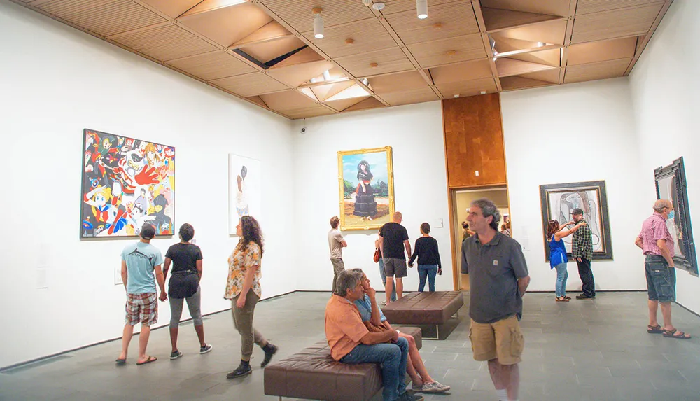 Visitors are viewing and discussing various artworks in a spacious well-lit modern art gallery