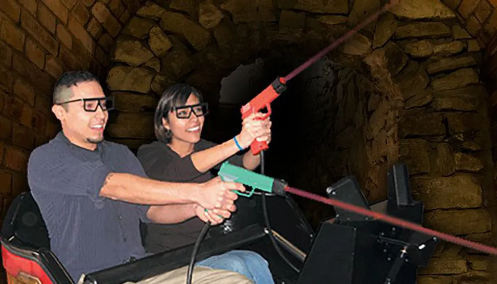 Two people are smiling and wearing 3D glasses seemingly enjoying a ride or attraction where they hold a toy gun together against a backdrop that resembles a stone tunnel