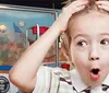 A surprised young child is wide-eyed and holding their head with their mouth open in front of a backdrop featuring the Guinness World Records logo