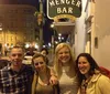 A group of people is posing for a photo at night in front of the historic Alamo mission in San Antonio Texas with one individual holding a Ghost Walk sign suggesting they may be participating in a ghost tour event