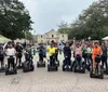 A group of people wearing helmets and riding Segways are waving cheerfully in front of a historic building
