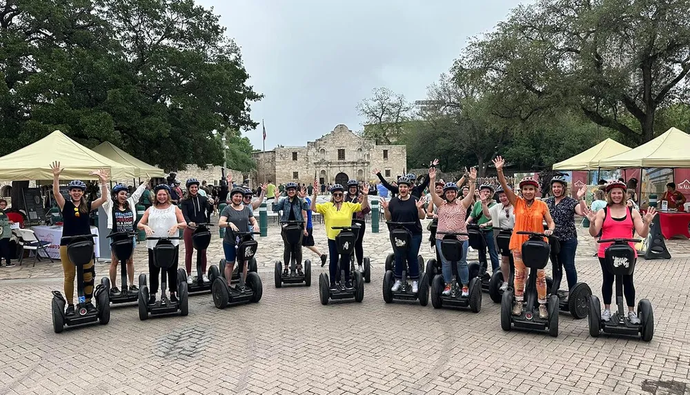 A group of people wearing helmets and riding Segways are waving cheerfully in front of a historic building