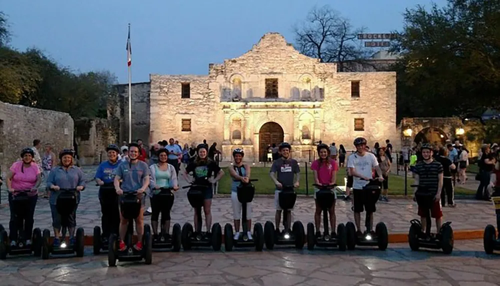 A group of people are posing on Segways in front of The Alamo at dusk