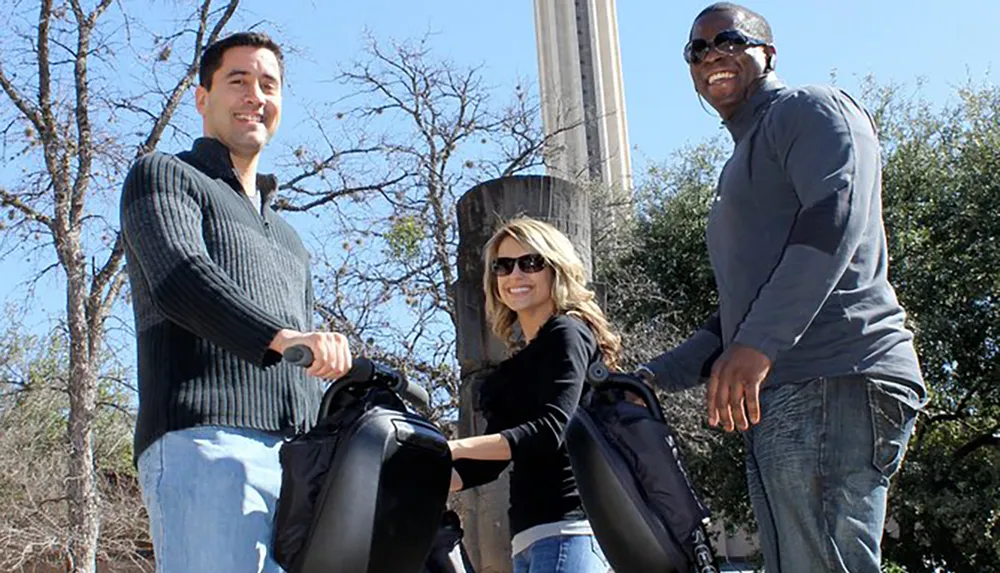 Three people are standing outdoors smiling and each is handling a handlebar of Segway-like personal transporters on a sunny day