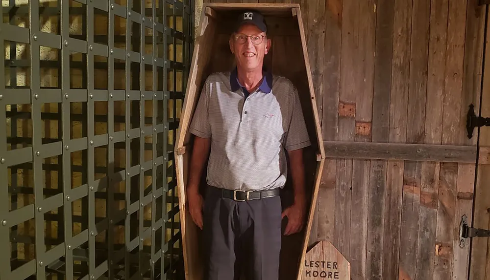 A smiling man stands in a wooden coffin-shaped photo opportunity spot with the name Lester Moore on a sign below it